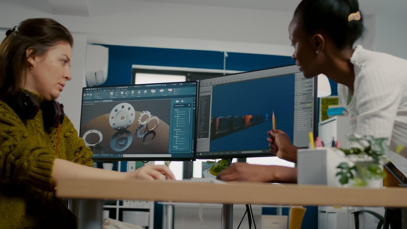 Two engineers reviewing a 3D CAD model on dual monitors in a modern workspace